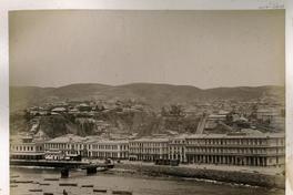 [Vista general de Valparaíso desde el muelle fiscal, en el mar se divisan botes y en el fondo lo cerros]