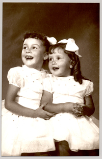 [Dos hermanas sentadas riéndose con vestido mangas cortas englobadas y bordados de colores y cintas blancas en el pelo]