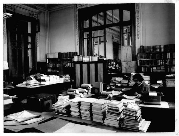 [Biblioteca Nacional, vista general de la oficina catalogación, con dos personas trabajando]