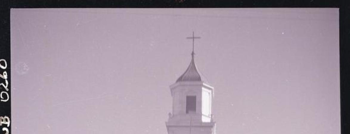 [Niña con un burrito que lleva carga, pasa frente a una capilla]