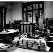 [Biblioteca Nacional, vista general de la oficina catalogación, con dos personas trabajando]