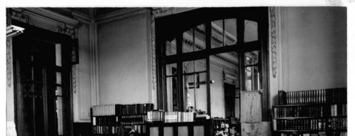 [Biblioteca Nacional, vista general de la oficina catalogación, con dos personas trabajando]