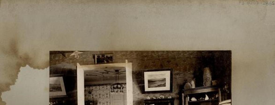 [Hombre sentado frente a su escritorio, de madera noble, divido en gavetas; alrededor de la habitación, cuadros y anaqueles que exhiben minerales]