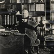 [Andrés Bello sentado leyendo en un escritorio con una biblioteca de fondo]