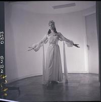 [Bailarina de ballet, caracterizada para una obra, posando de pié con los brazos extendidos]