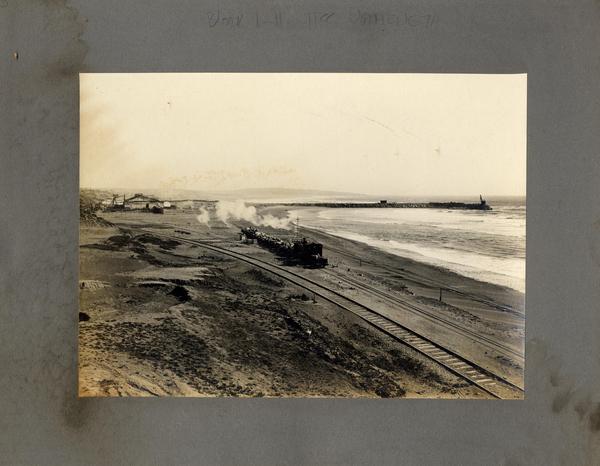 [Vista de una locomotora de carga, pasando por la orilla del mar]