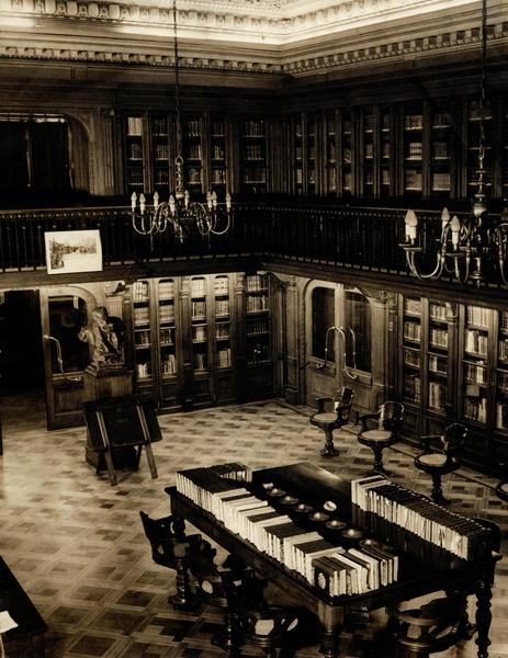 [Vista interior de la Biblioteca Americana Barros Arana, Sala Medina, Biblioteca Nacional: espacio revestido en madera de nogal, Anaqueles con puerta de vidrio, parquet de maderas nobles, lámparas de techo en bronce, de 8 brazos con bombillas como velas, balconada en el segundo piso, busto de Barros Arana]