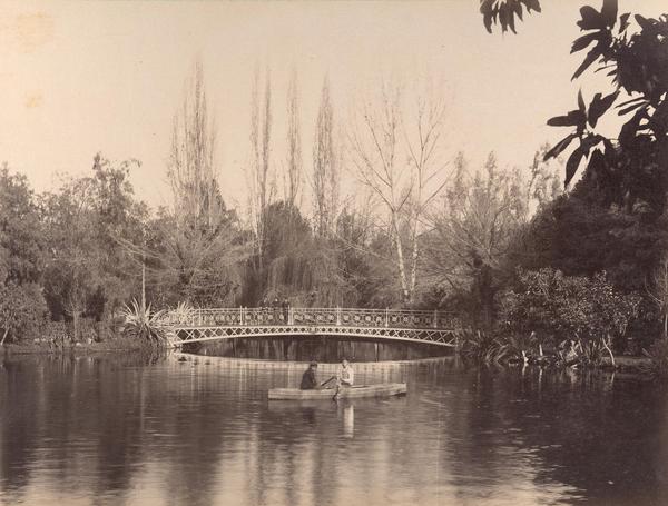 [Laguna : con bote y dos personas; y con un puente de fondo en un bosque]