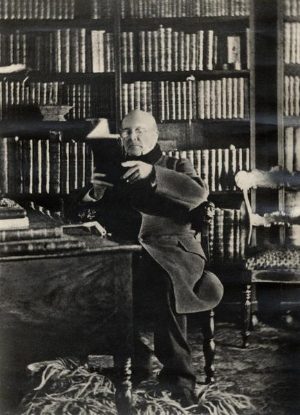 [Andrés Bello sentado leyendo en un escritorio con una biblioteca de fondo]