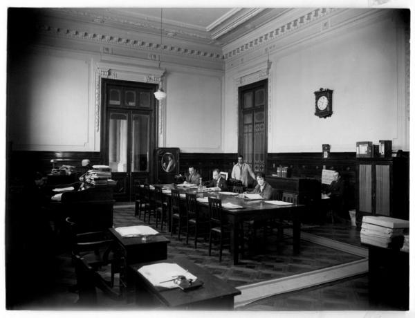 [Biblioteca Nacional 1927. Salones interiores, con una mesa rectangular y cuatro personas]