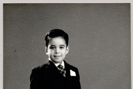 [Niño vestido con terno oscuro de pantalón corto, corbata, pañuelo blanco en el bolsillo y un camión de juguete en el suelo]