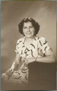 [Mujer morena sonriente, sentada y apoyada en un sillón de estudio]