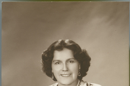 [Mujer morena sonriente, sentada y apoyada en un sillón de estudio]