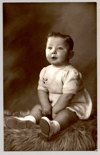 [Niñito rubio de ojos azules, con traje de hilo, zapatos y soquetes blancos sentado sobre un felpudo]