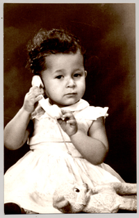 [Niñita de pelo corto ondulado, vestido blanco amplio, hablando por teléfono]
