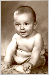 [Bebé con un traje de hilo con el pecho y piernas descubiertas sentado sobre un felpudo]