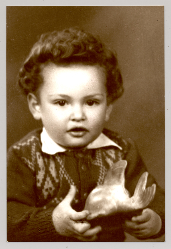 [Niñito pelo onduldo, chaleco abotonado con dibujos,camisa cuello blanco con una figura en sus manos]