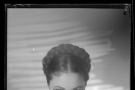 [Mujer joven, peinada con una trenza alrededor de su cabeza, sus manos cruzadas sobre el pecho, sostienen dos pequeños rostros esculpidos en bronce]