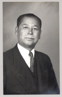 [Hombre de rasgos algo asiático traje oscuro y corbata a rayas]