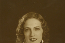 [Mujer joven, vestida elegantemente con una blusa blanca de seda, pelo risado, labios rojos, aros grandes y un collar en su cuello]