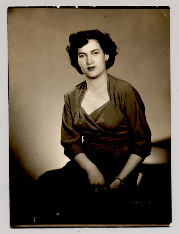 [Mujer morena de pelo ondulado y vestido oscuro posando sentada]